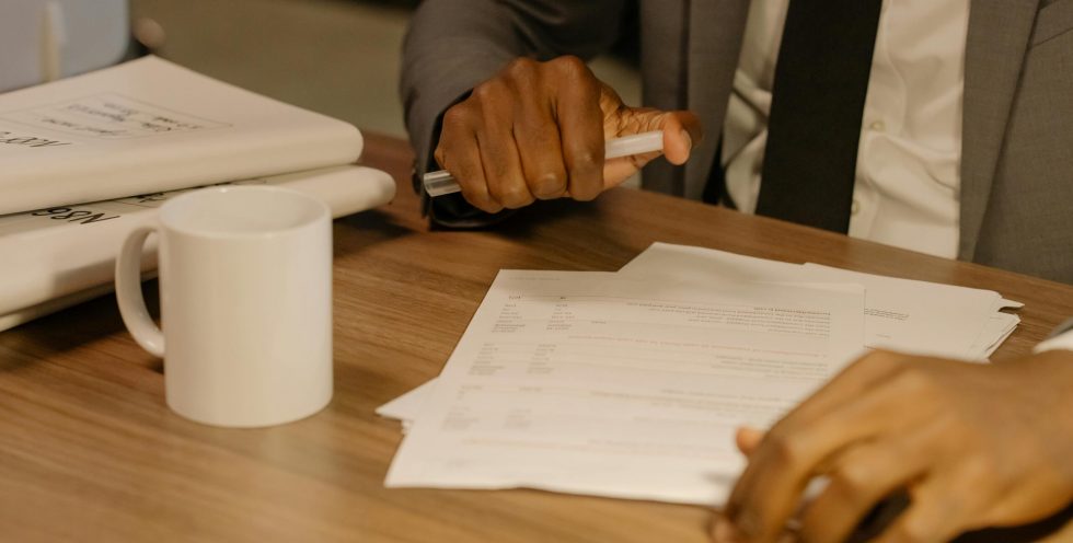 Free Close-up of a businessman holding and reviewing documents on a wooden desk. Stock Photo
