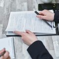 Free Close-up of hands analyzing insurance policy paperwork with pen on table. Stock Photo