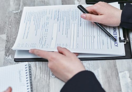Free Close-up of hands analyzing insurance policy paperwork with pen on table. Stock Photo