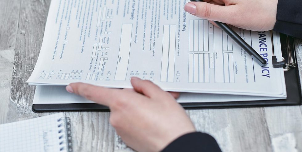 Free Close-up of hands analyzing insurance policy paperwork with pen on table. Stock Photo
